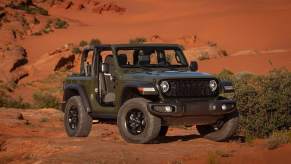 A dark-gray 2024 Jeep Wrangler Willys 2-door parked in front of a dusty red hill