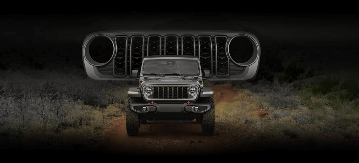 A front shot of a 2024 Jeep Wrangler compact SUV parked on a off-road trail with its grille superimposed above