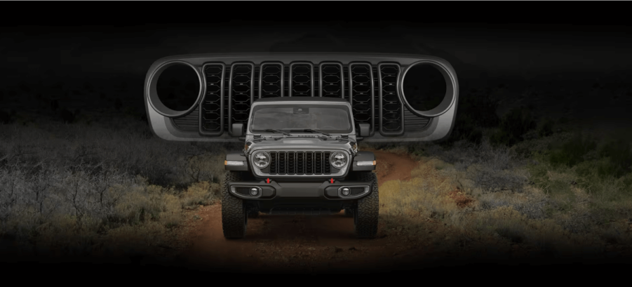 A front shot of a 2024 Jeep Wrangler compact SUV parked on a off-road trail with its grille superimposed above