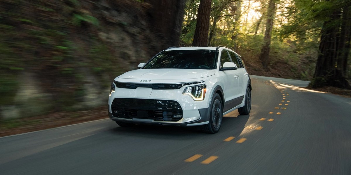 A white 2024 Kia Niro EV subcompact electric SUV is driving on the road.