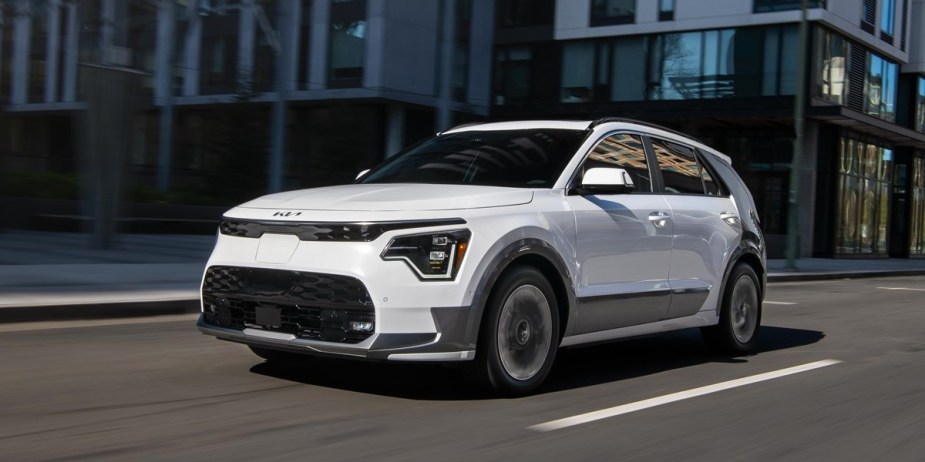 A white 2024 Kia Niro EV subcompact electric SUV is driving on the road. 
