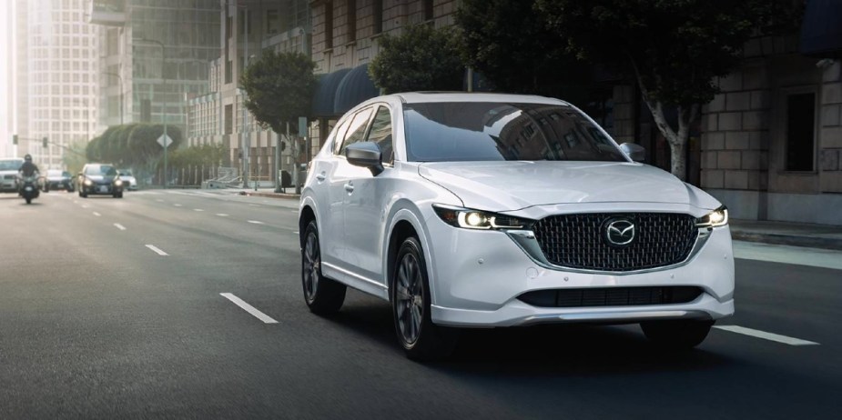 A white 2024 Mazda CX-5 small SUV is driving on the road. 