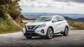 A white 2024 Nissan Murano midsize SUV parked on gravel overlooking mountains on a cloudy day