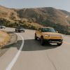 Three Rivian R1T models driving along a curved road by a cliff. The 2024 Rivian R1T is becoming a contender.