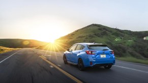 The 2024 Subaru Impreza RS trim level in blue driving into the sunrise on a road by a hill.
