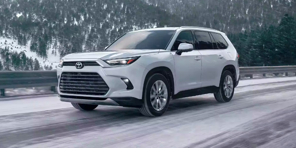 A white 2024 Toyota Grand Highlander midsize three-row SUV is driving on a snowy road.