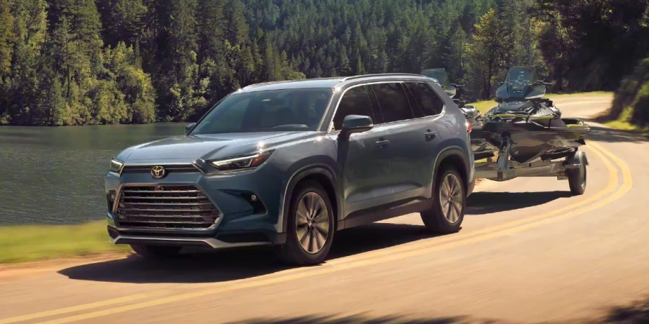 A blue 2024 Toyota Grand Highlander Hybrid MAX is driving while towing a jet ski. 