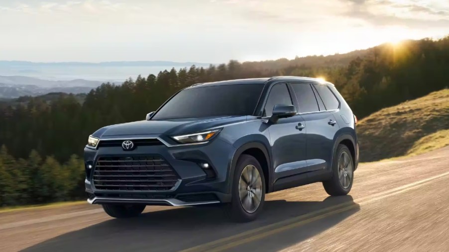 A blue 2024 Toyota Grand Highlander midsize three-row SUV is driving on the road.