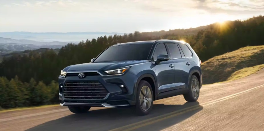 A blue 2024 Toyota Grand Highlander midsize three-row SUV is driving on the road. 