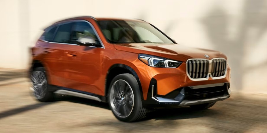 An orange BMW X1 subcompact luxury SUV is driving. 