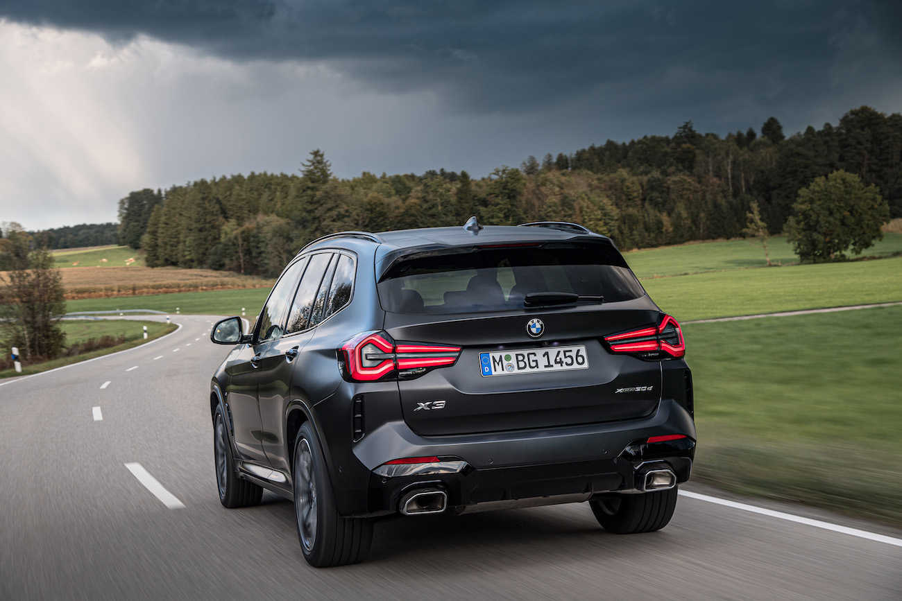 The rear of a black BMW X3 driving on a stormy road. The BMW X3's price isn't that bad compared to others in the class.