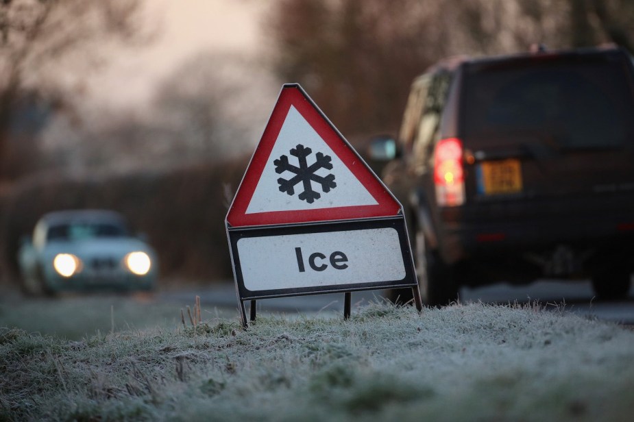 Two cars pass an Ice caution sign on a rural road.