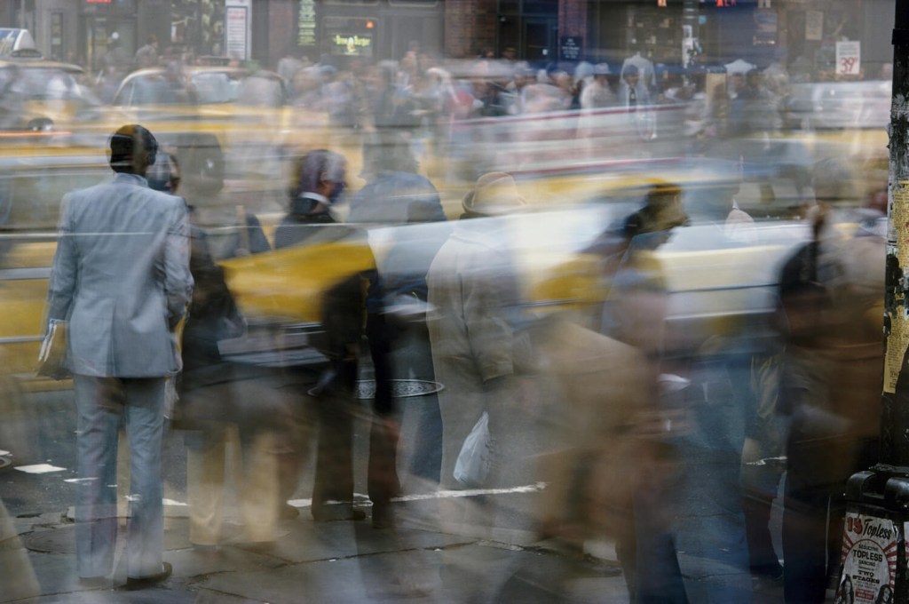 Pedestrians and yellow taxis passing through a busy city intersection.