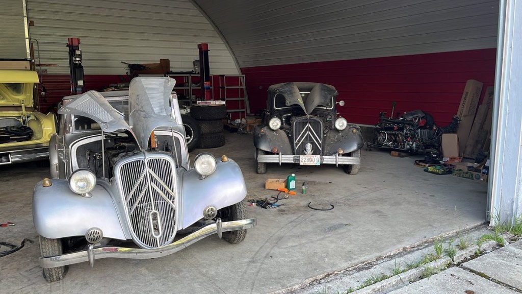 A pair of Citroens sitting with the hoods open in a barn. 