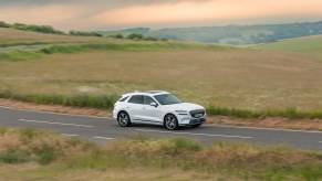 A white Electrified Genesis GV70 driving along a winding road. Genesis service offers plenty of perks for owners.