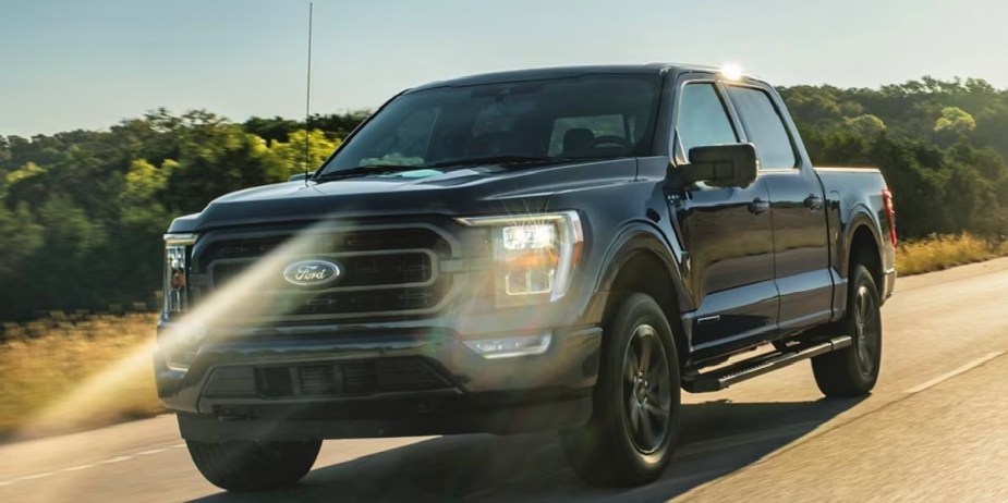 A black Ford F-150 full-size pickup truck is driving on the road. 