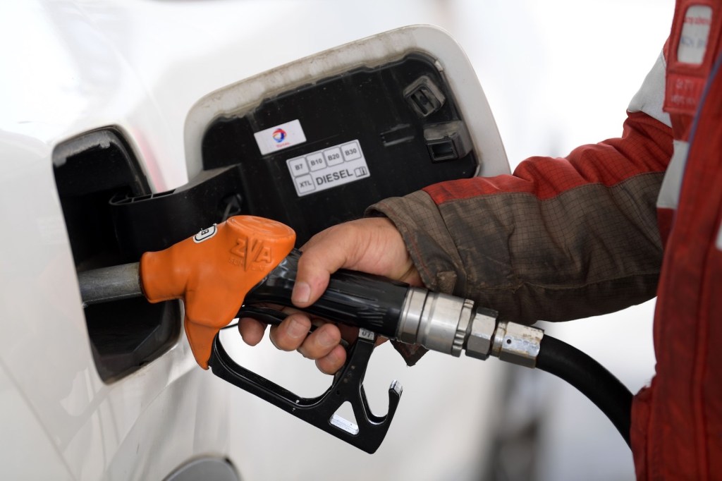The hand of a man holding an orange gasoline nozzle to pump fuel into his car or truck.