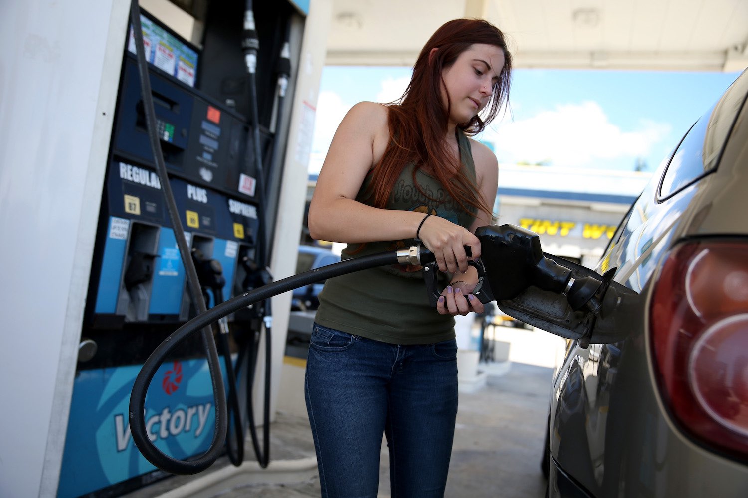 A woman fills her gas tank at a fuel pump.
