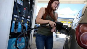 A woman fills her gas tank at a fuel pump.