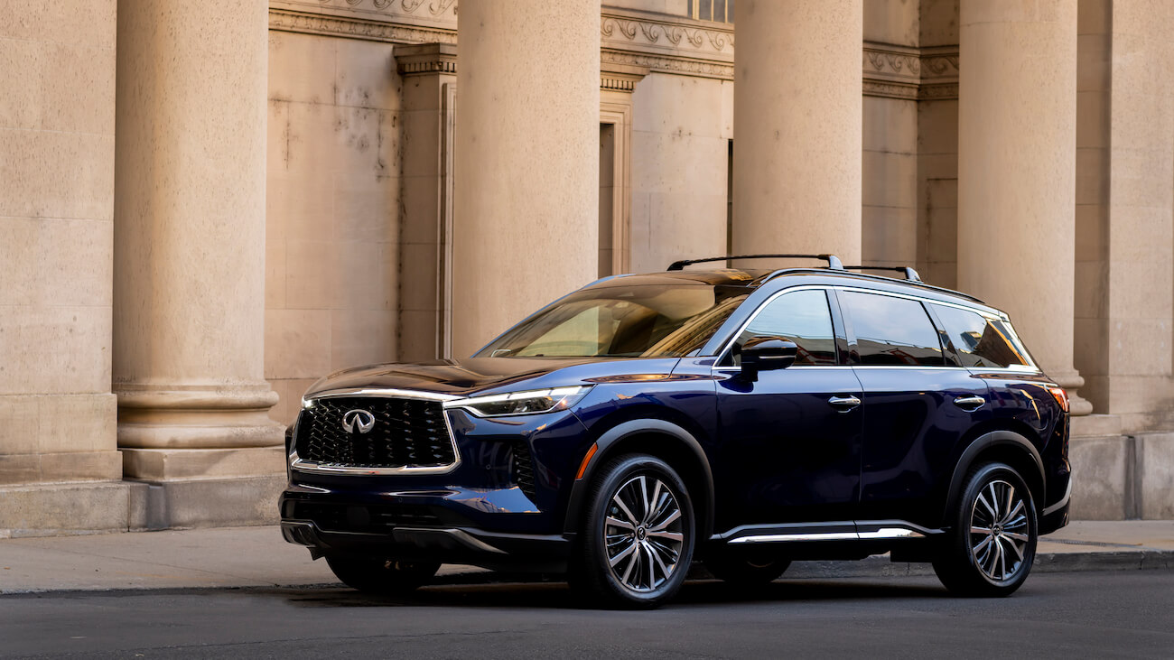The 2024 Infiniti QX60 in blue parked in front of a historical building with pillars. Infiniti sales are low compared to competitors.