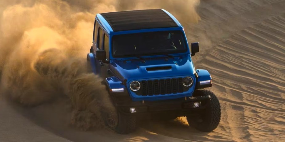 A blue Jeep Wrangler small SUV is driving off-road. 