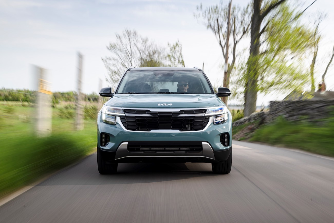 A 2024 Kia Seltos in Photon Blue speeding down a country road. This Kia SUV offers a ton of value
