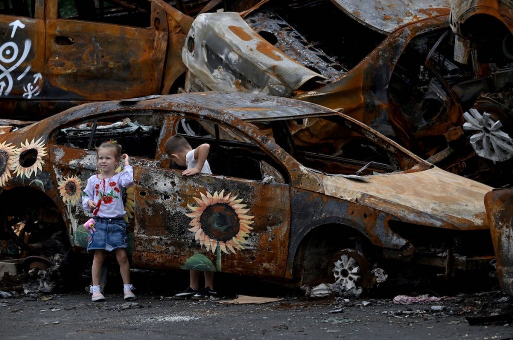 Two kids playing in a burned out car in a junk yard. 