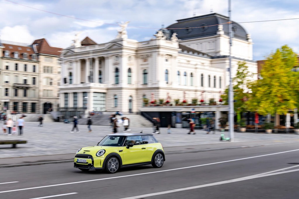 A yellow Mini Cooper S drives down a road