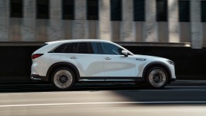 A white Mazda CX-90 driving down a city road. The CX-90 is the most expensive Mazda.