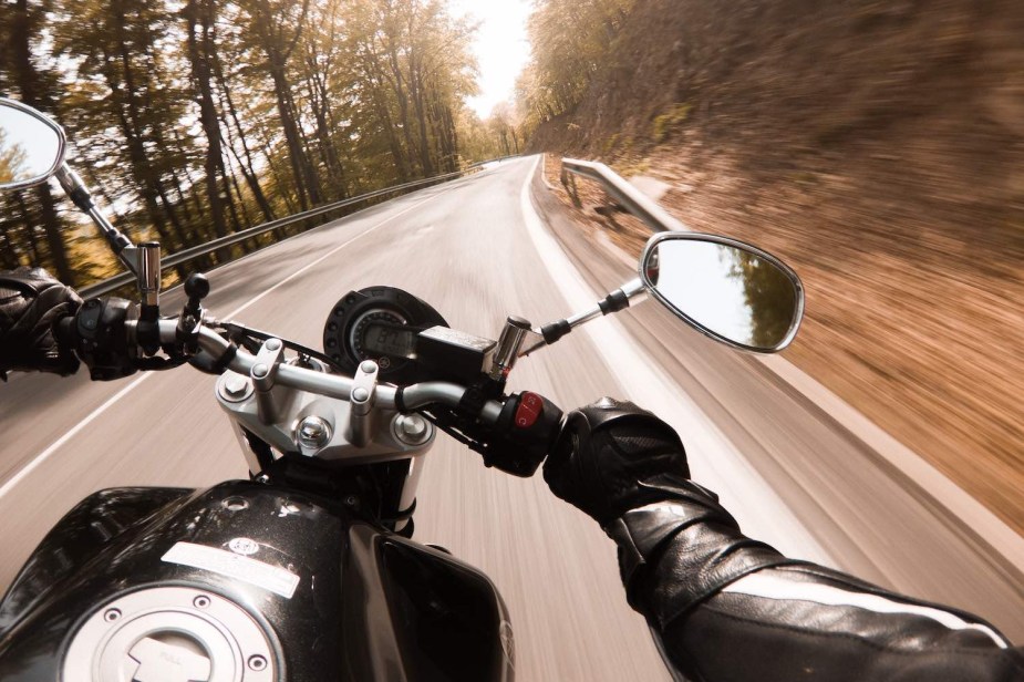 The handlebars of a motorcycle navigating a tight corner in the Adirondack mountains.