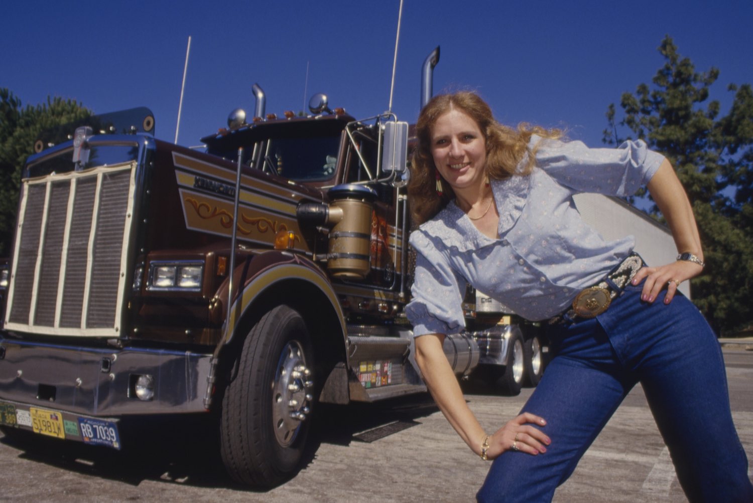 A female truck driver from Nebraska stands next to her big rig parked in California.
