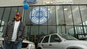 A man standing in front of a new car dealership in the 1990s.