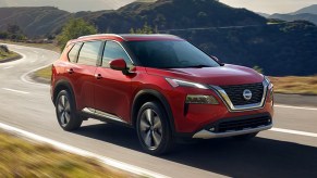 A red 2023 Nissan Rogue small SUV is driving on the road.