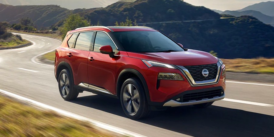 A red 2023 Nissan Rogue small SUV is driving on the road.