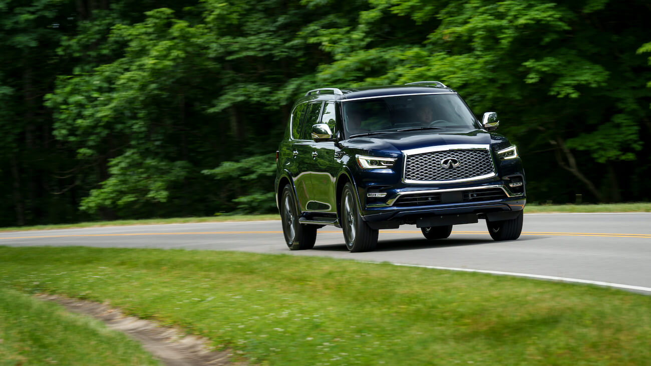 A black 2024 Infiniti QX80 driving on a forest road. Nissan's luxury brand is struggling this year.