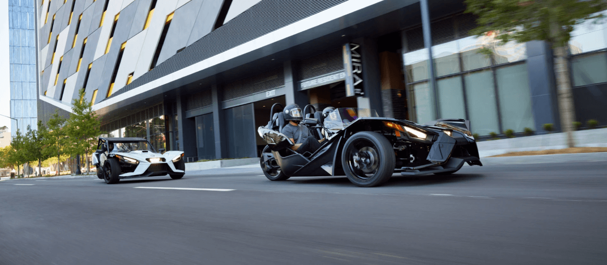A pair of Polaris Slingshot three-wheeler models racing through a downtown city section and deserted street