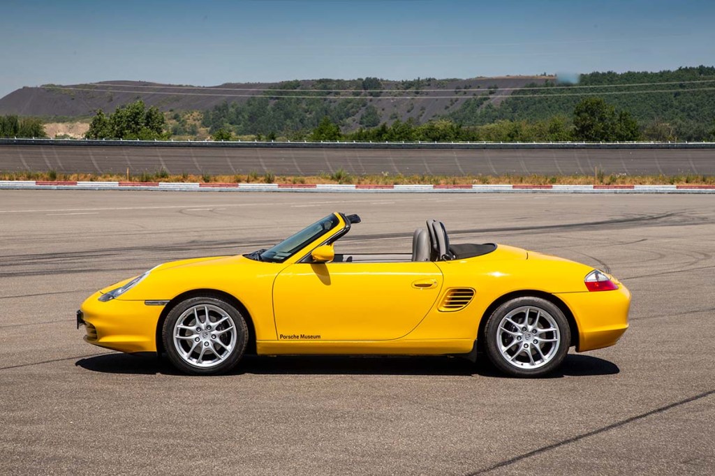 Side profile view of yellow Porsche 986 Boxster parked on race track