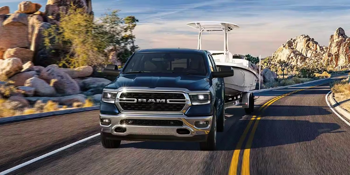 A blue Ram 1500 full-size pickup truck is driving on the road. 