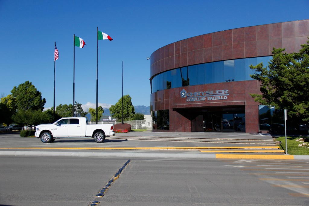 White heavy-duty Ram 3500 pickup truck parked under a Mexico flag in front of the Saltillo factory.