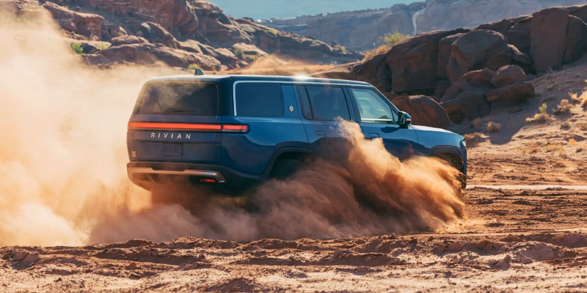A blue Rivian R1S electric SUV is driving off-road.