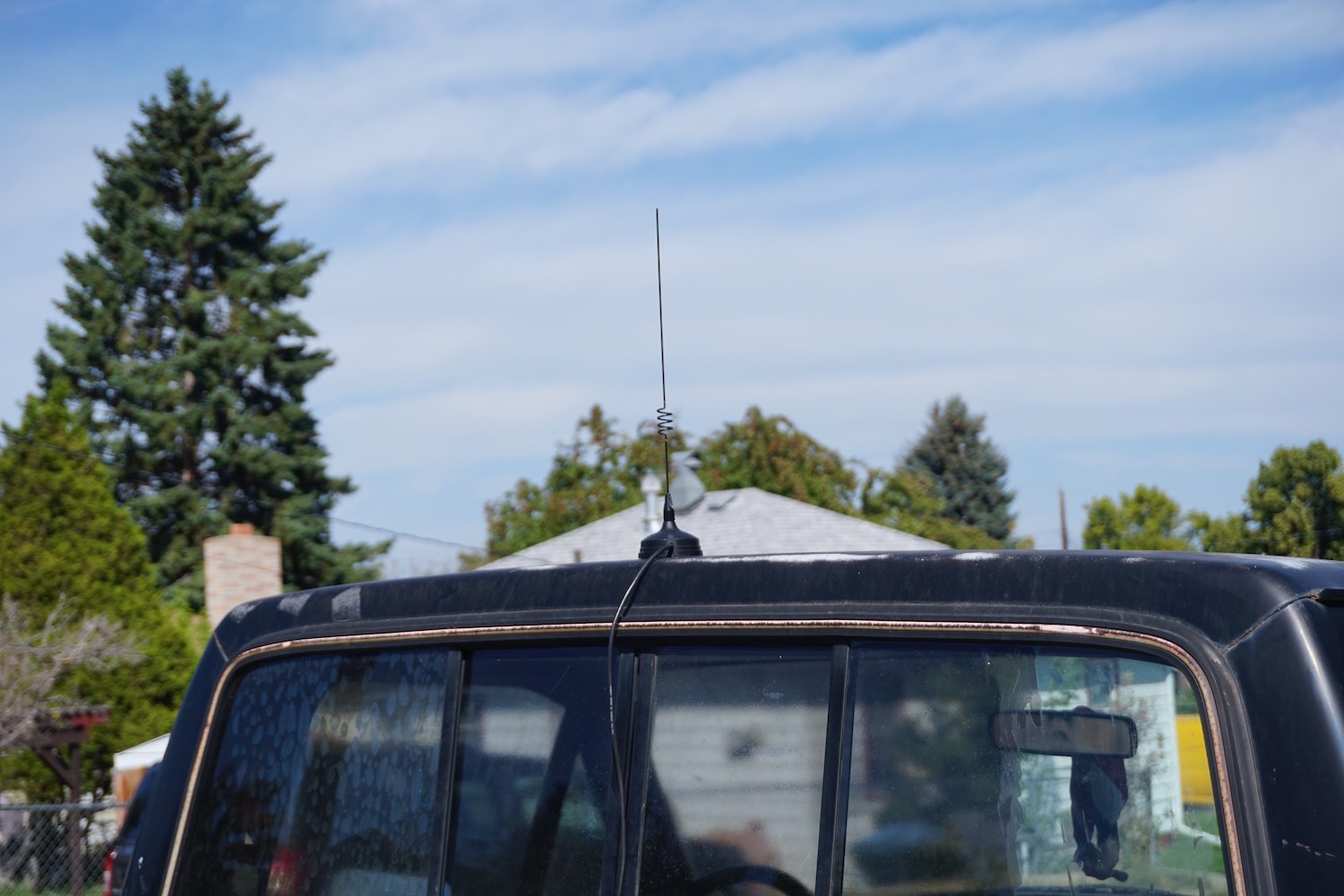 Magnetic CB radio whip antenna on the roof of a black pickup truck, blue sky in the background.