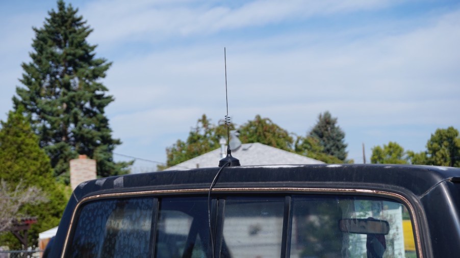 Magnetic CB radio whip antenna on the roof of a black pickup truck, blue sky in the background.