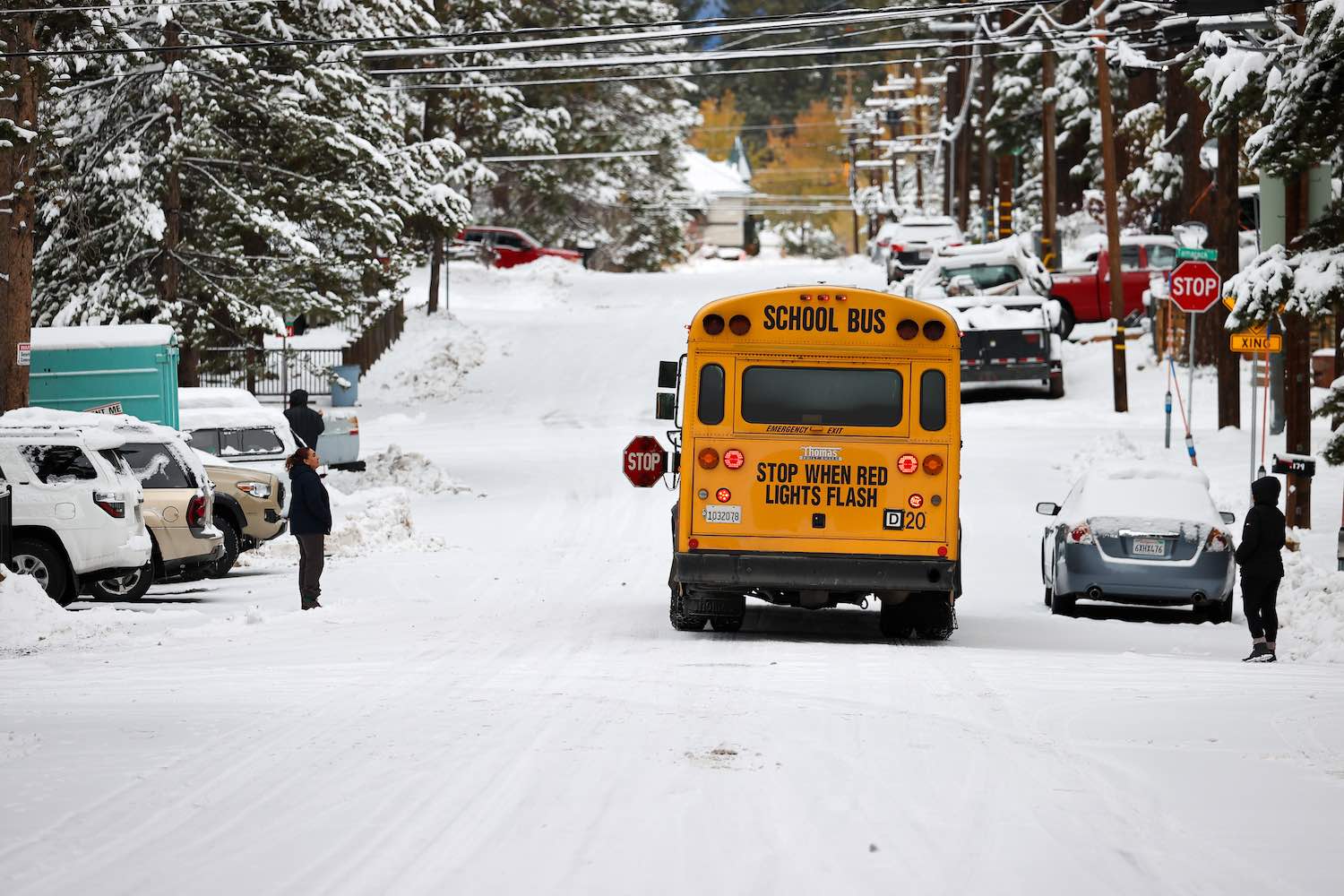 Parents watch students get on a school bus parked on a snowy street.