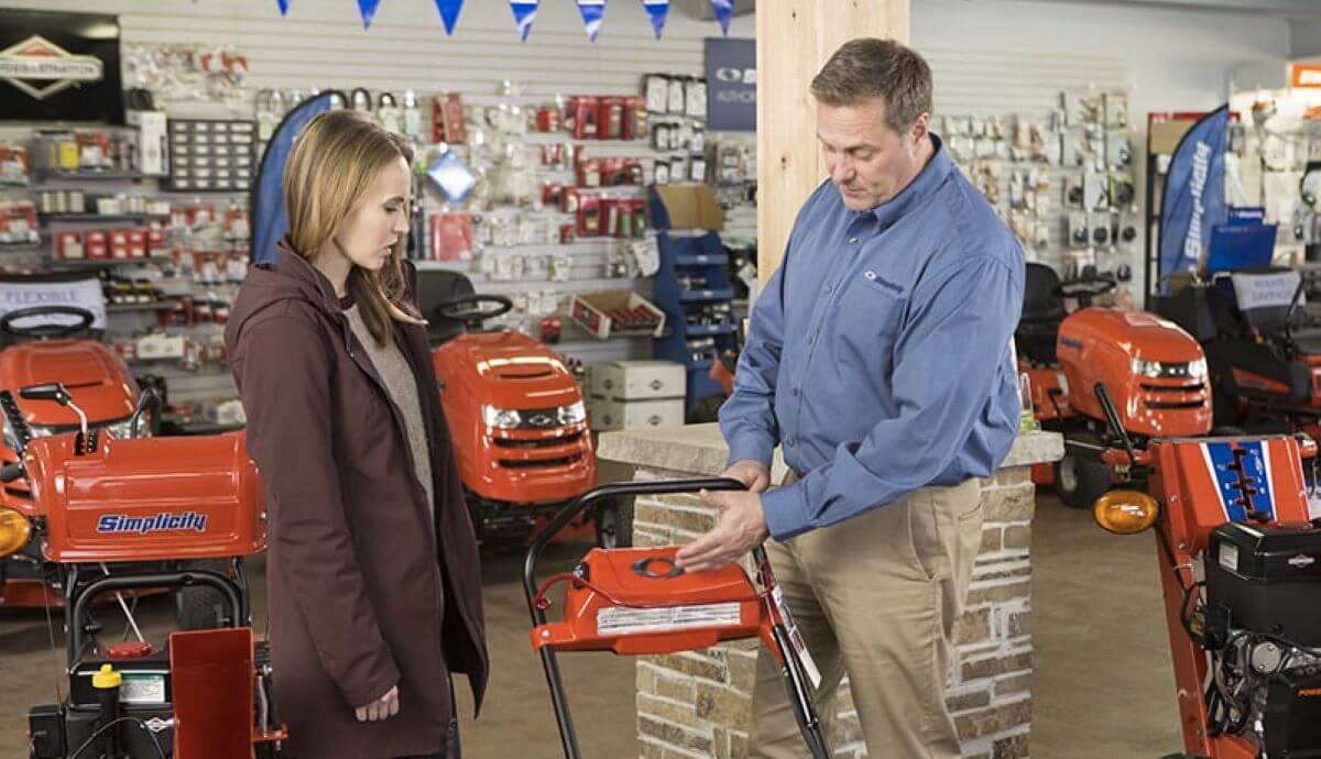 A salesman pitching a lawn mower model to a potential customer inside a Briggs & Stratton Simplicity store section