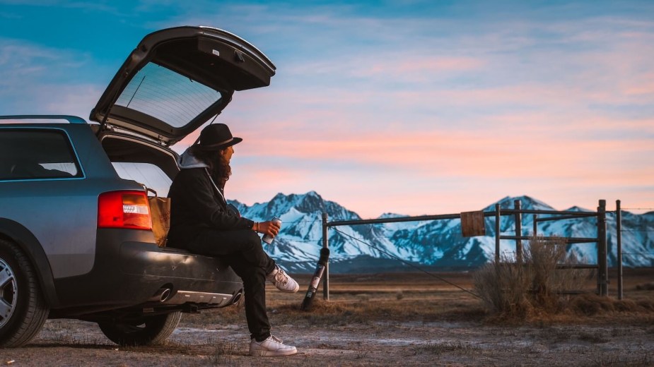 A man watched the sunset from the bumper of his station wagon while holding a beer.