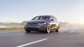 Gray Tesla Model X driving down a road. Tesla advertising is nonexistent.