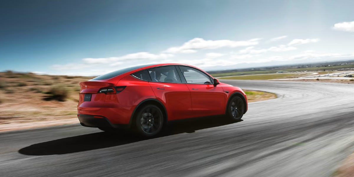 An orange Tesla Model Y small electric SUV is driving on the road.