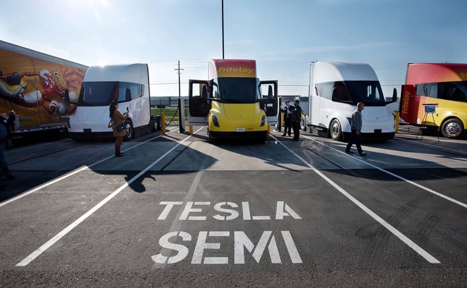 A row of PepsiCo's Tesla semi trucks in a parking lot, connected to chargers.