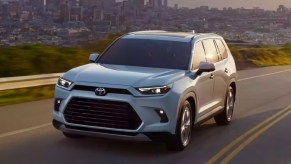 A white 2024 Toyota Grand Highlander midsize three-row SUV is driving on the road.