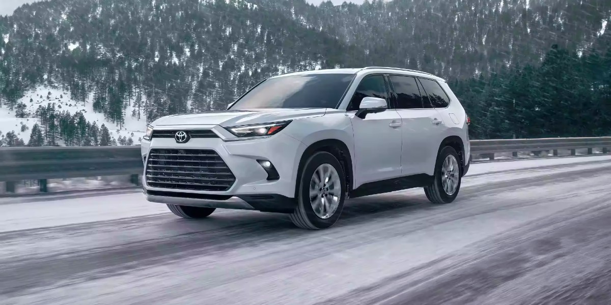 A white 2024 Toyota Grand Highlander Hybrid is driving on a snowy road.